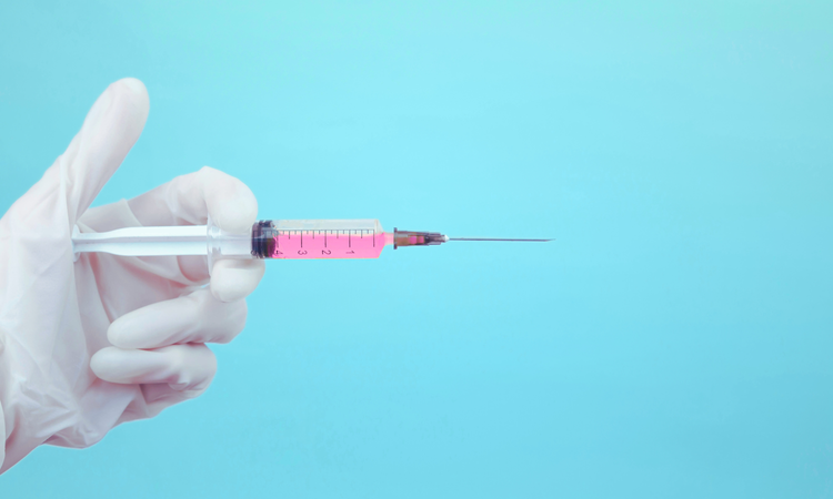 Hand in white latex glove holding a syringe with pink liquid on light blue background.