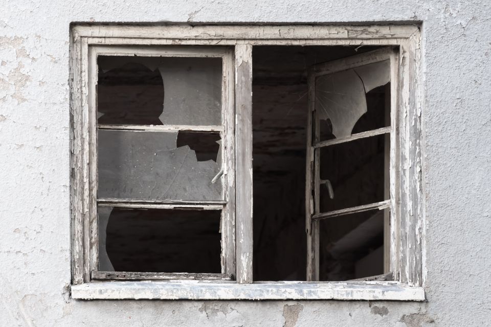 Image of broken window, cement house, gray and white with broken glass.